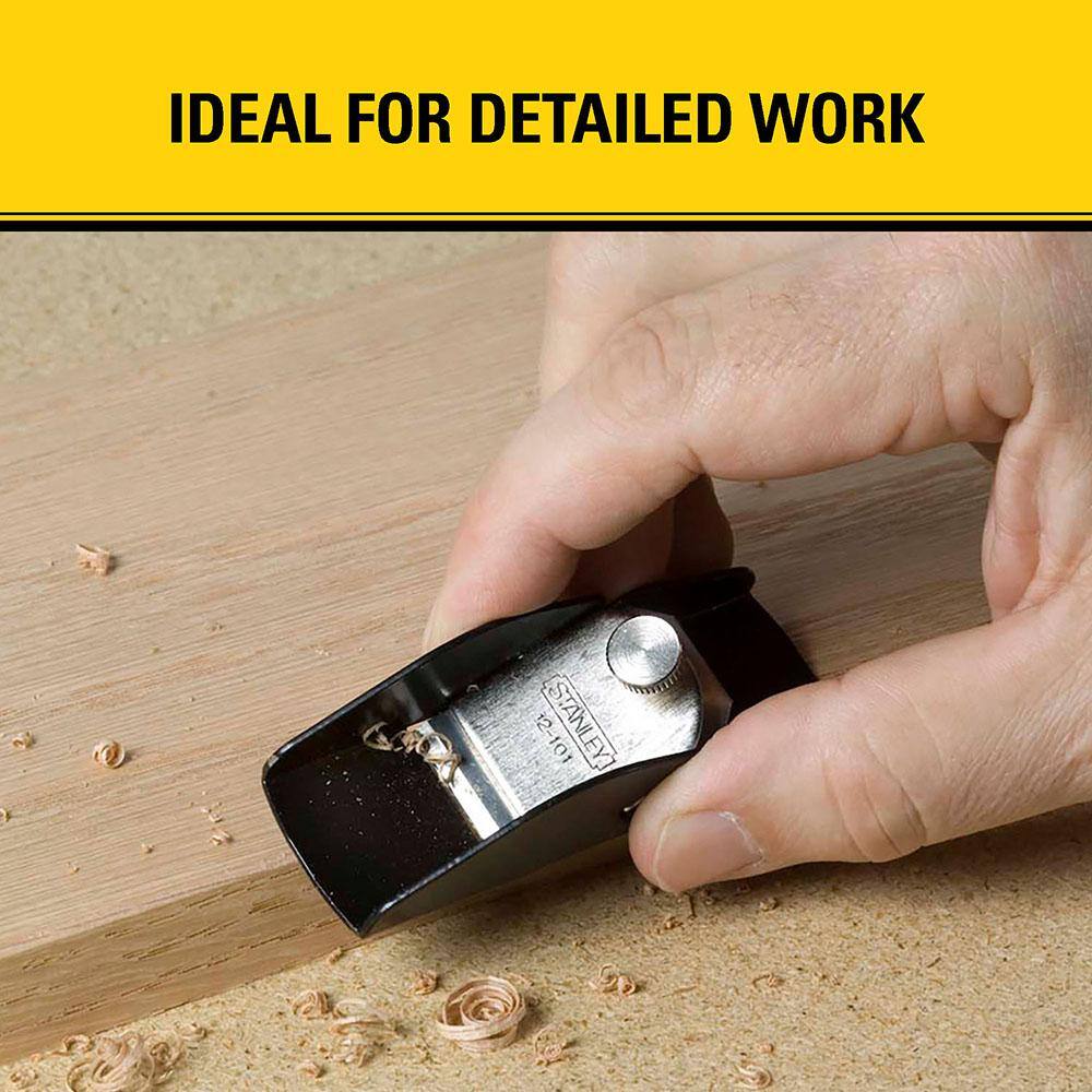 A worker manually manipulating a STANLEY 12-101 miniature trimming pocket plane across a soft timber workpiece to produce clean wood curls beneath a marketing banner reading ideal for detailed work.