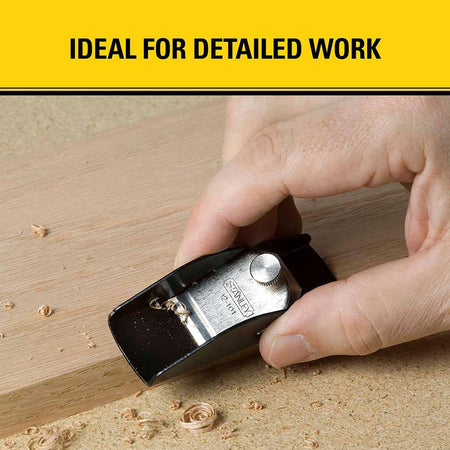 A worker manually manipulating a STANLEY 12-101 miniature trimming pocket plane across a soft timber workpiece to produce clean wood curls beneath a marketing banner reading ideal for detailed work.