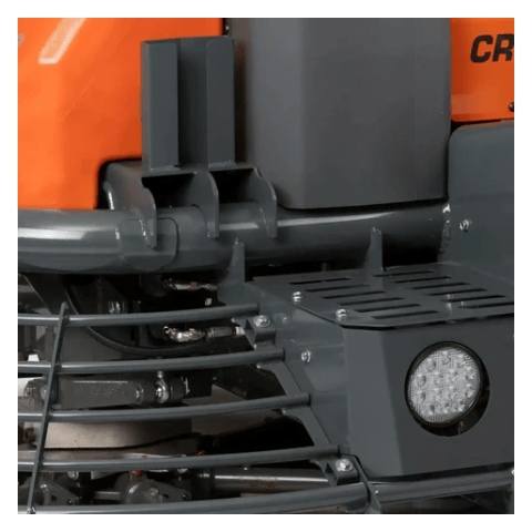 The image shows a close-up view of a Husqvarna 59" Riding Power Trowel CRT 60 74LX. It highlights the machine's features, including the operator's area with the seat, control levers, and handles, along with a portion of the orange fuel tank. The safety cage surrounding the rotating trowel blades is also visible.