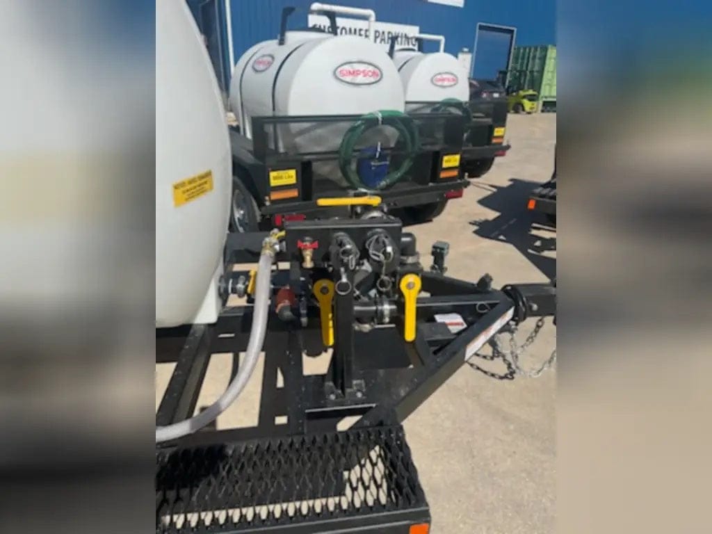 A front-facing view of the Simpson 95404 trailer's mounting platform, showing the intake and discharge ports, safety chains, and the reinforced A-frame hitch for secure towing.