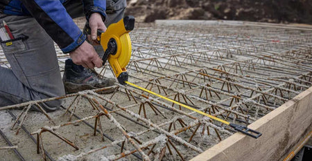 Construction worker measuring across a rebar grid using a Stabila long‑distance tape measure, illustrating accurate layout alignment and professional‑grade measurement capability for reinforced concrete foundation preparation.
