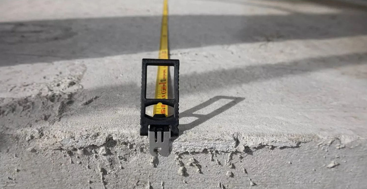 Close‑up of a yellow measuring tape stretched across a rough concrete surface, showing high‑contrast imperial markings and secure end hook placement for accurate distance measurement in construction and layout applications.