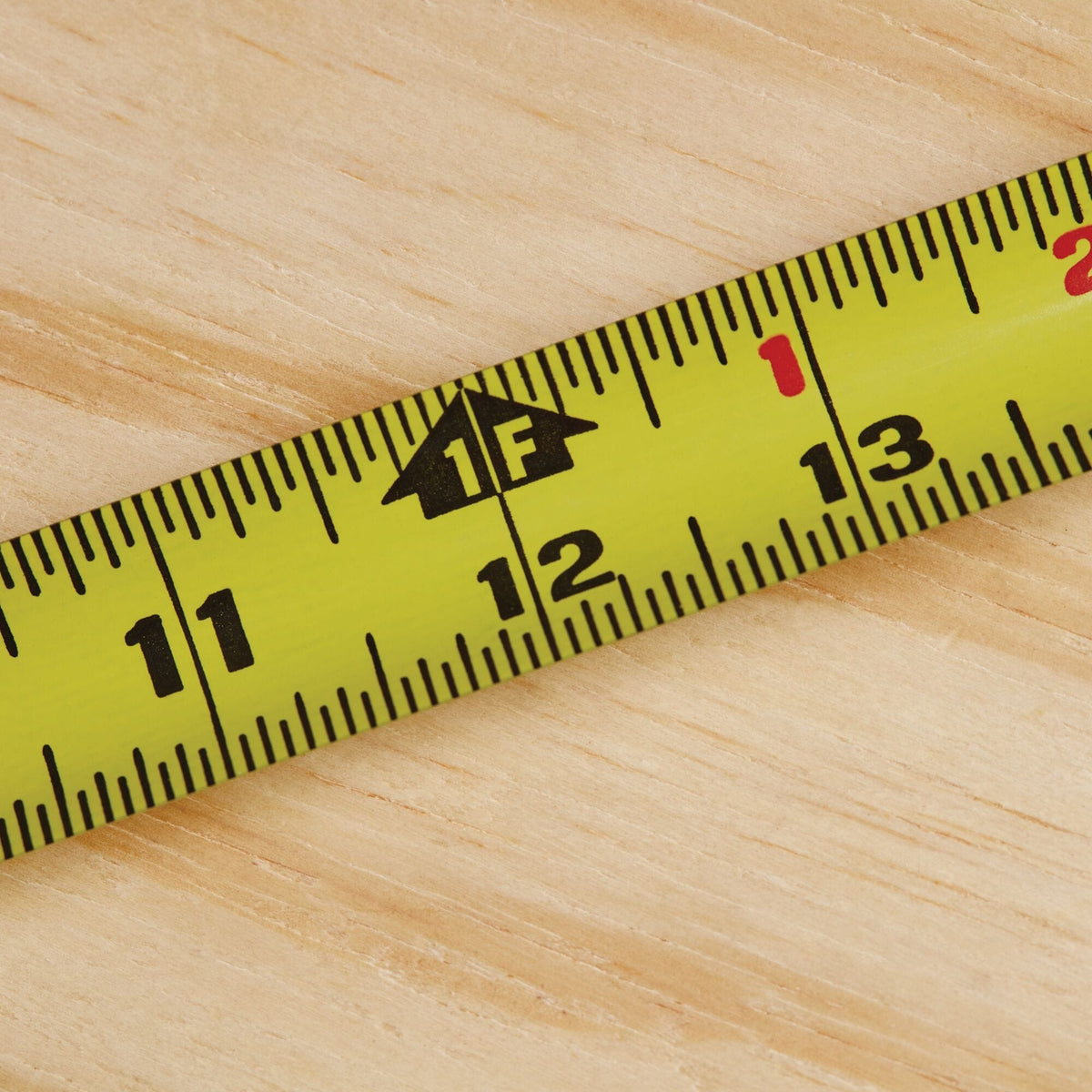 A macro close-up photograph tracking the yellow steel blade of the Stanley PowerLock 25-foot tape rule, focusing on the 12-inch milestone highlighted by a distinct black arrow graphic indicating one linear foot.