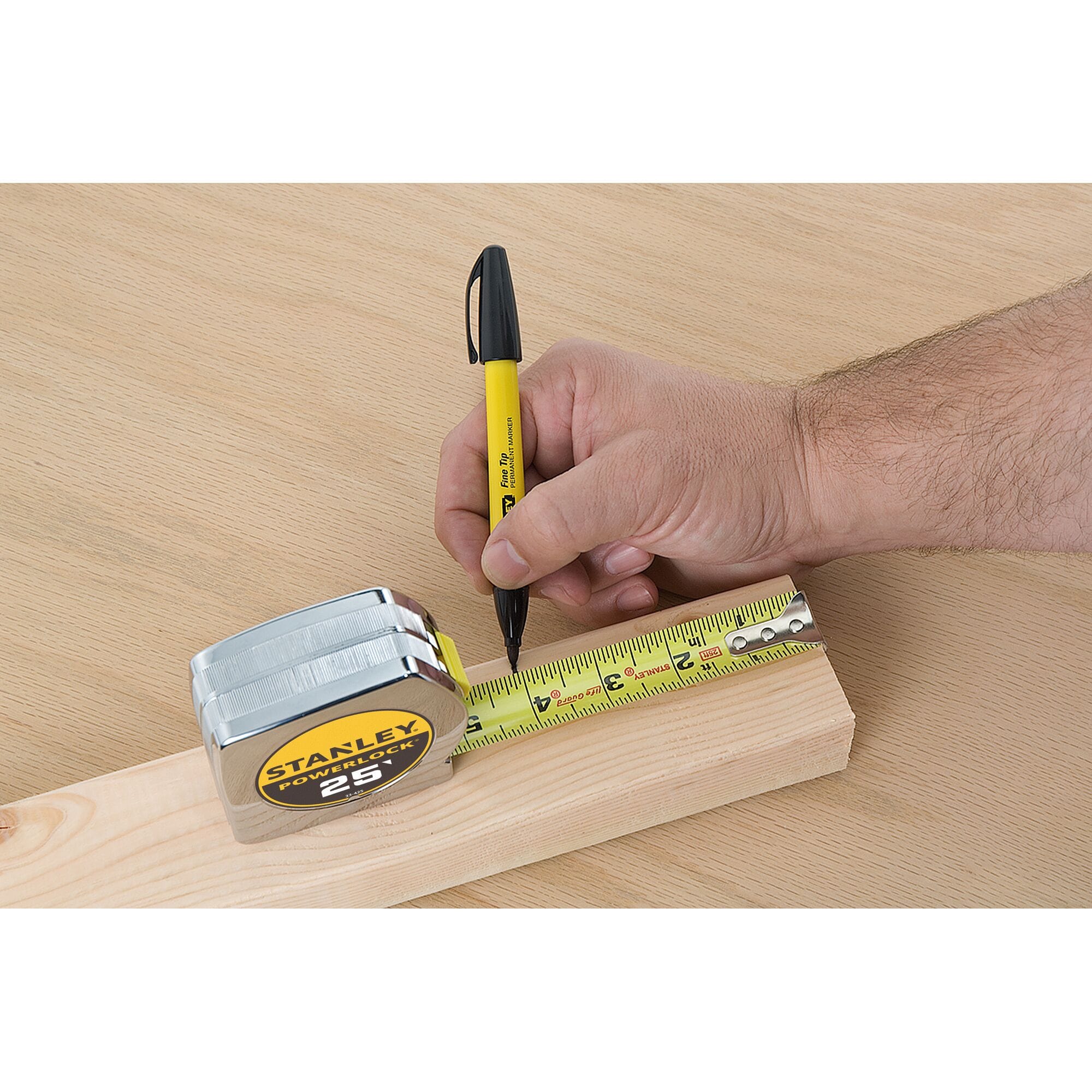 A close-up studio lifestyle photo of a technician using a yellow fine-tip permanent marker to trace a precise dimension tick mark along the extended high-contrast steel blade of the Stanley PowerLock tape rule over lumber.
