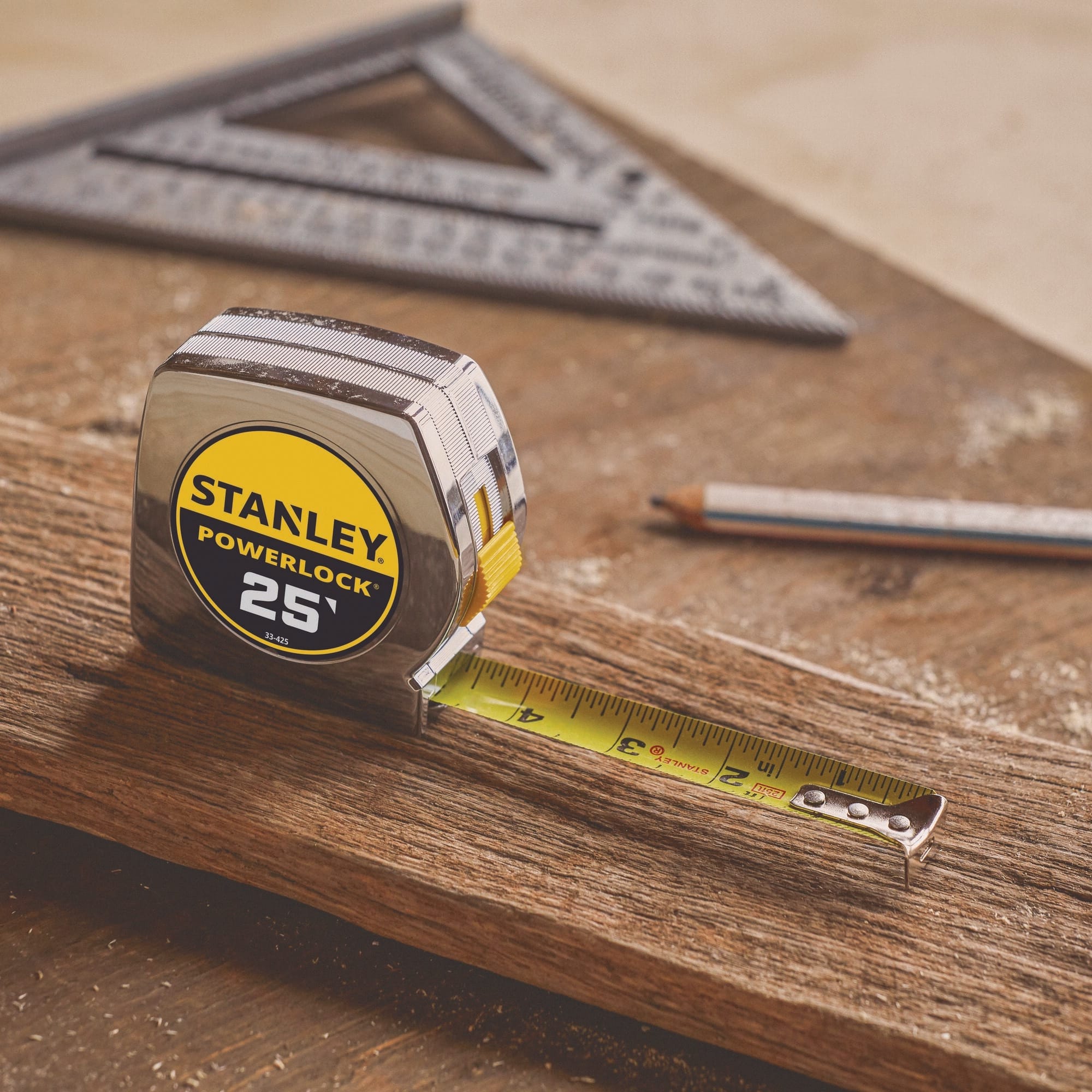 A close-up professional product shot of the Stanley PowerLock 25-foot tape measure resting face-forward on a rustic timber beam with its yellow blade slightly extended next to a carpenter's pencil and a metal speed square.