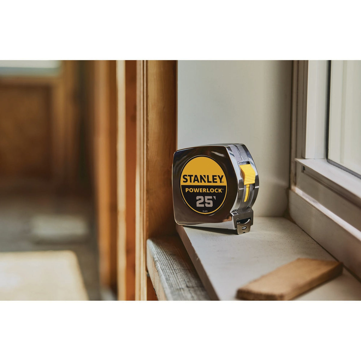 A real-world interior carpentry shot of the classic chrome-cased Stanley PowerLock measuring tool sitting upright on a white-painted wooden windowsill inside a house currently under renovation.