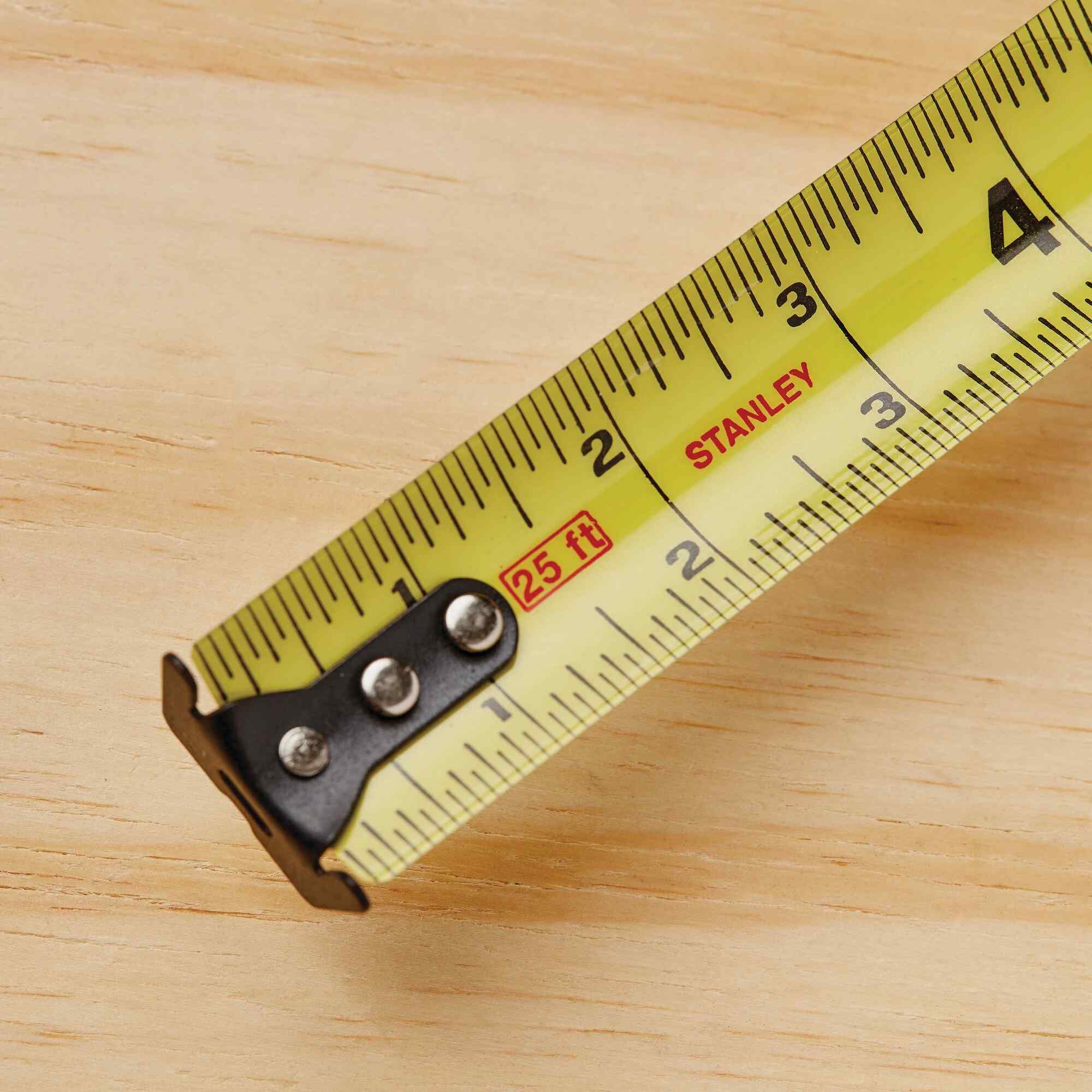 A top-down view of the first four inches of the Stanley FATMAX 30 ft tape measure blade, emphasizing the high-contrast black numbers, red stud center markings, and the reinforced three-rivet multi-catch hook.