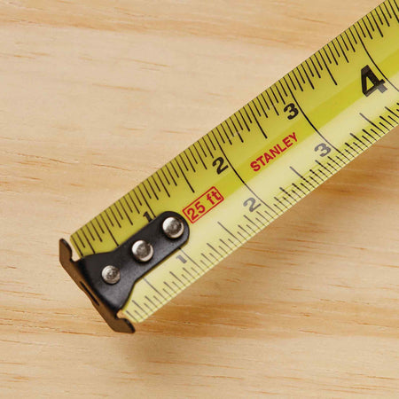 A top-down view of the first four inches of the Stanley FATMAX 30 ft tape measure blade, emphasizing the high-contrast black numbers, red stud center markings, and the reinforced three-rivet multi-catch hook.