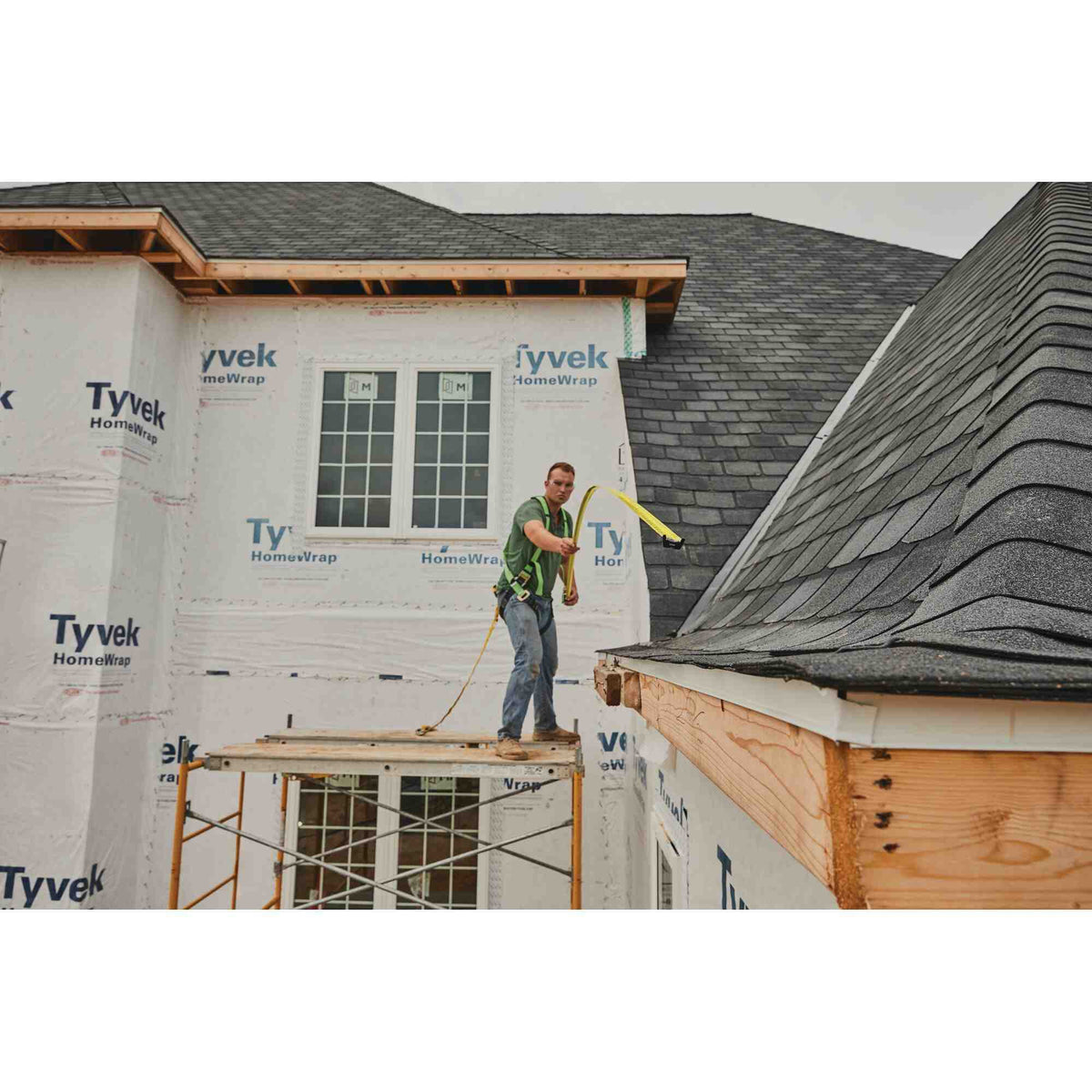 A professional tradesman standing on scaffolding using the 11 foot standout feature of the Stanley 33-735 tape measure to reach across a residential roofing project safely.