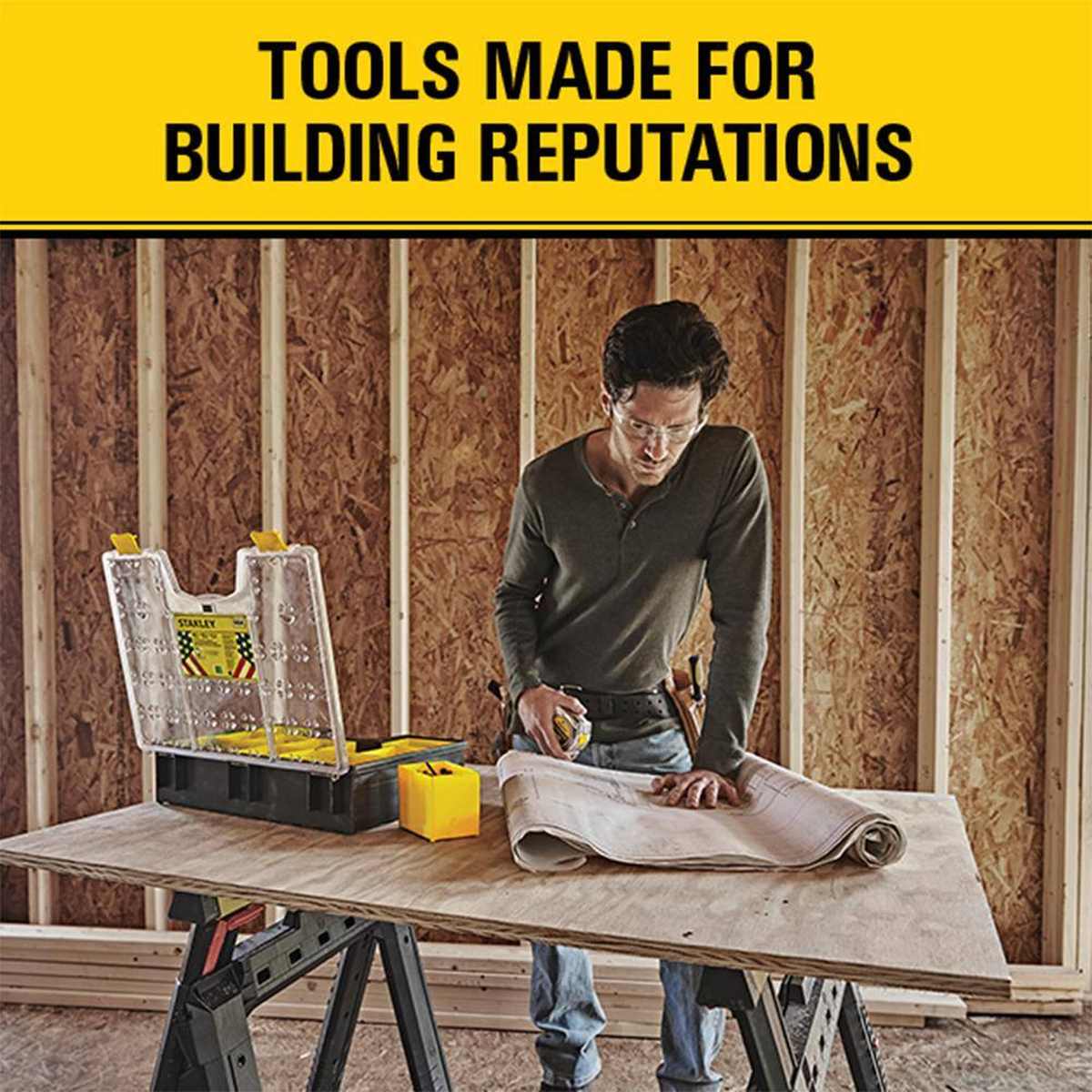 Lifestyle image of a professional builder using the Stanley FATMAX tape measure while reviewing architectural blueprints on a jobsite workbench.