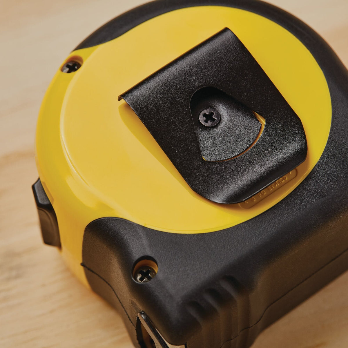 A macro close-up photograph of the back of the yellow and black Stanley FatMax layout tool casing, highlighting the attached black spring-tempered steel belt clip secured into position with a central recessed screw.