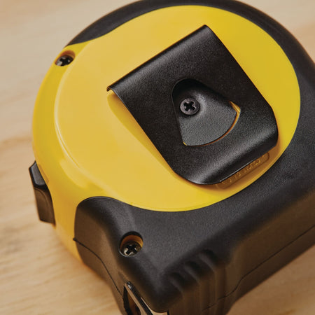 A macro close-up photograph of the back of the yellow and black Stanley FatMax layout tool casing, highlighting the attached black spring-tempered steel belt clip secured into position with a central recessed screw.