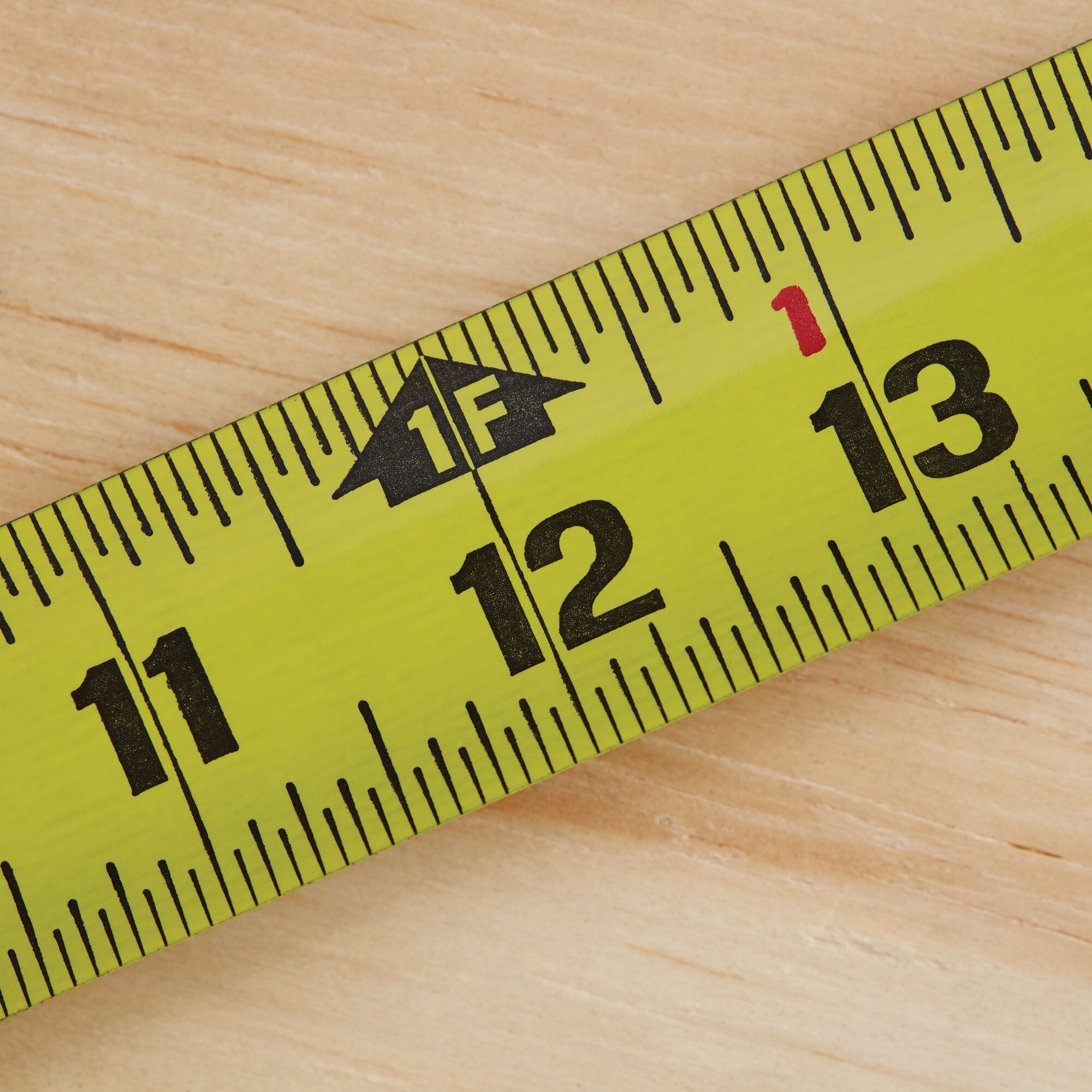 A close-up studio shot tracking across the high-tensile steel blade of the Stanley FatMax rule, focusing on the high-visibility 12-inch milestone highlighted by a distinct black arrow graphic indicating one linear foot.