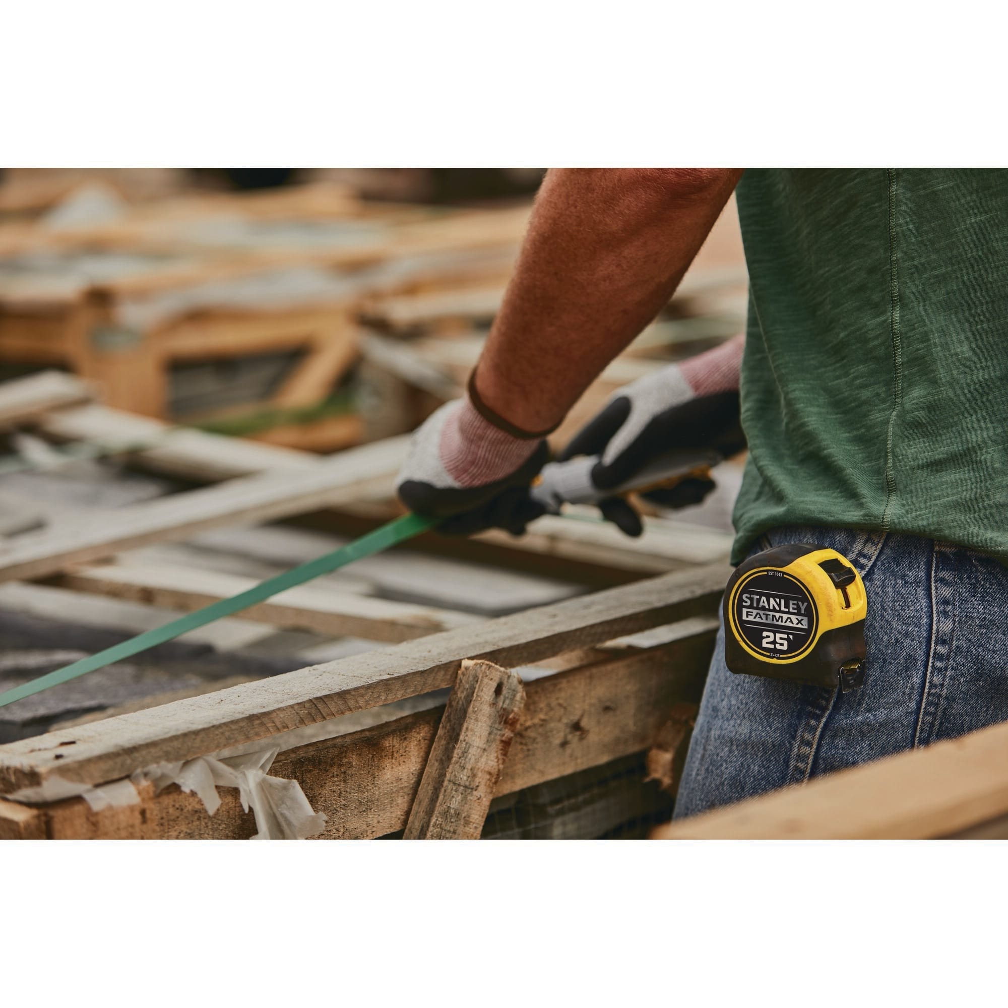 A mid-section lifestyle layout shot showing the yellow and black Stanley FatMax 25' measuring tape clipped securely to the back pocket of a worker's denim jeans on an outdoor construction yard site.