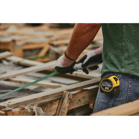 A mid-section lifestyle layout shot showing the yellow and black Stanley FatMax 25' measuring tape clipped securely to the back pocket of a worker's denim jeans on an outdoor construction yard site.