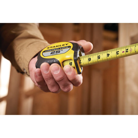 A perspective lifestyle shot of a contractor holding the yellow Stanley Control-Lock tape measure tool while extending the steel blade outward, highlighting the clear black numbers from 1 to 8 inches.