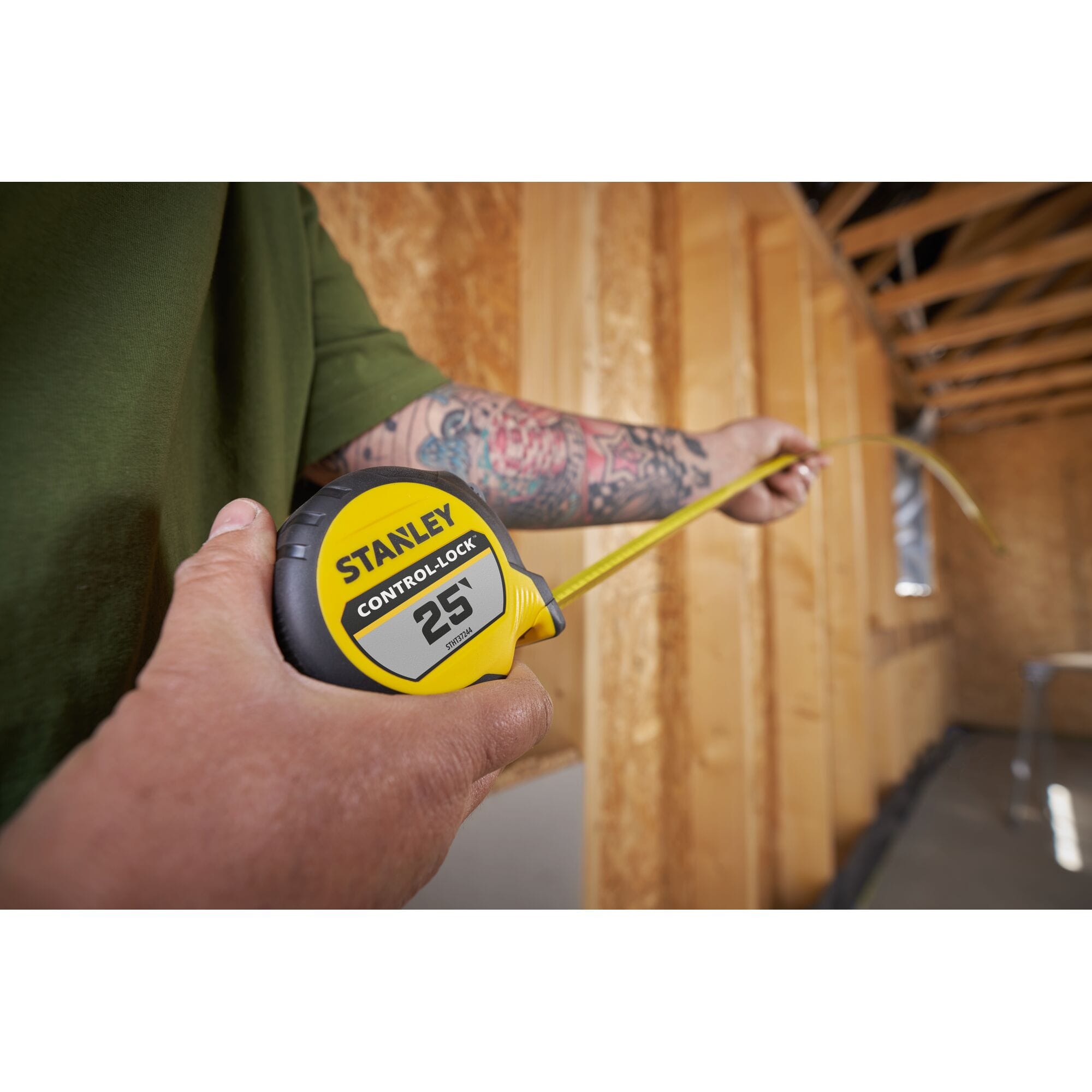 A jobsite layout application photograph highlighting a craftsman's hands testing the 12-foot standalone reach capacity by stretching the curved yellow steel blade horizontally across a wood wall framing cavity.