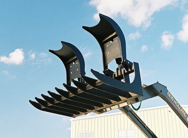 Low angle shot of the root grapple attached to a loader arm and raised against a blue sky, with both hydraulic claws fully extended open to demonstrate the vertical jaw range and tine spacing.