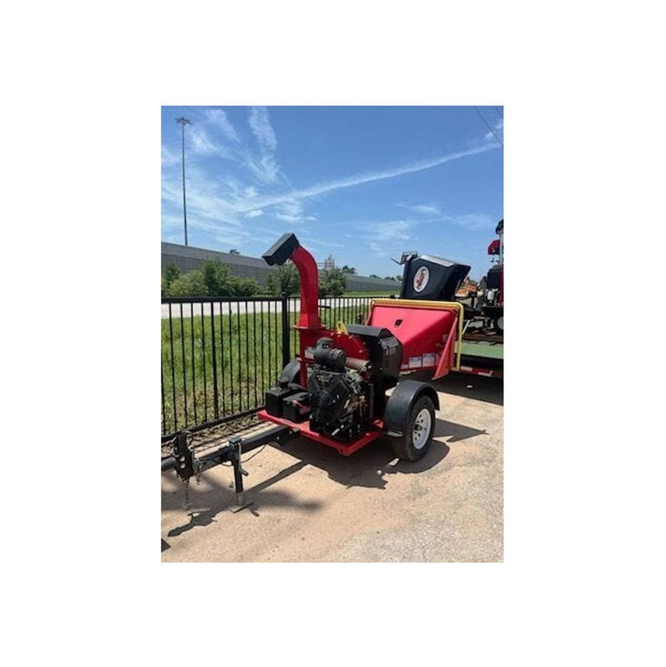 A side profile view of a red used 2021 Barreto 3107C wood chipper. The image shows the towable trailer frame with a single axle, the high-discharge chute, and the 31HP Briggs Vanguard engine, positioned outdoors against a black metal fence and a blue sky.
