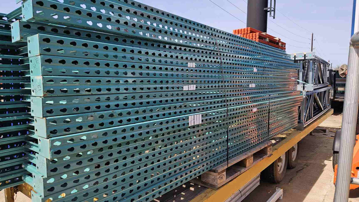 A wide side-profile view of a large stack of used like new green teardrop pallet rack uprights stored on a transport trailer, highlighting the 12-foot height and 36-inch depth with reinforced steel bracing for industrial warehouse storage.