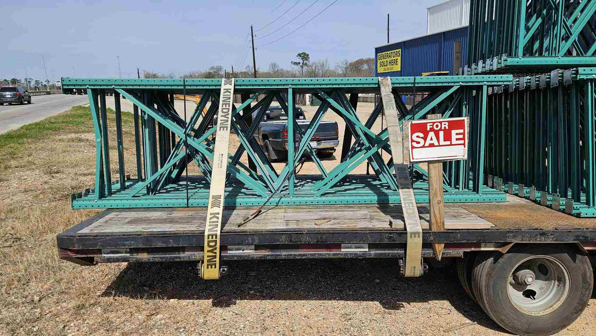 A side view of used like new green teardrop pallet rack uprights secured with straps on a transport trailer, highlighting the 12-foot height and 42-inch depth for industrial warehouse shelving.