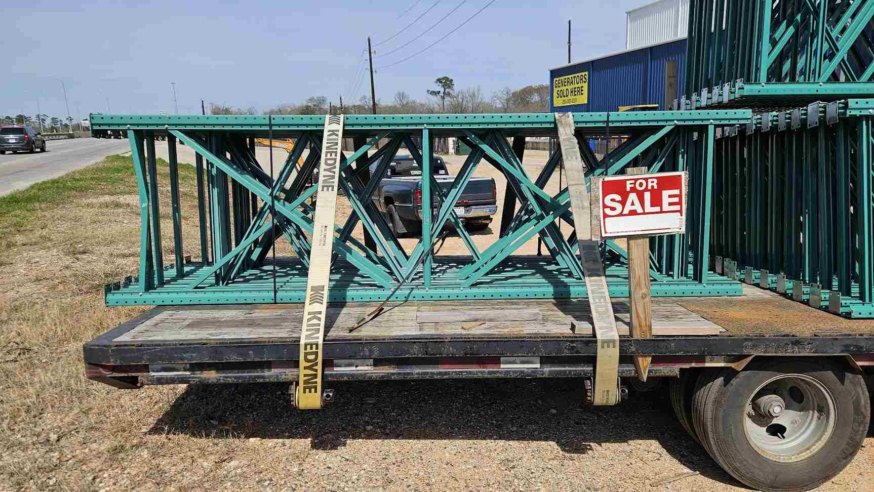 A side view of used like new green teardrop pallet rack uprights secured with straps on a transport trailer, highlighting the 12-foot height and 42-inch depth for industrial warehouse shelving.