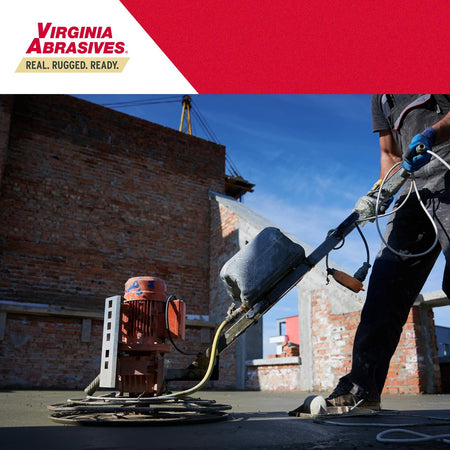 A worker on a construction site using a power trowel to finish a concrete floor on an upper level of a building.