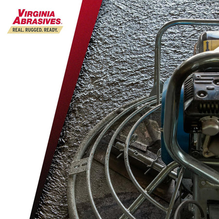 Close-up view of a power trowel's guard cage and blades rotating over a wet concrete surface during the finishing process.