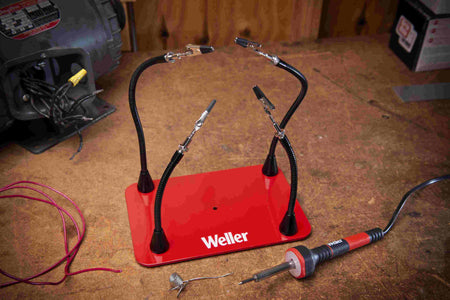 Weller helping hands tool on workbench with soldering iron and wires, used for electronics assembly.