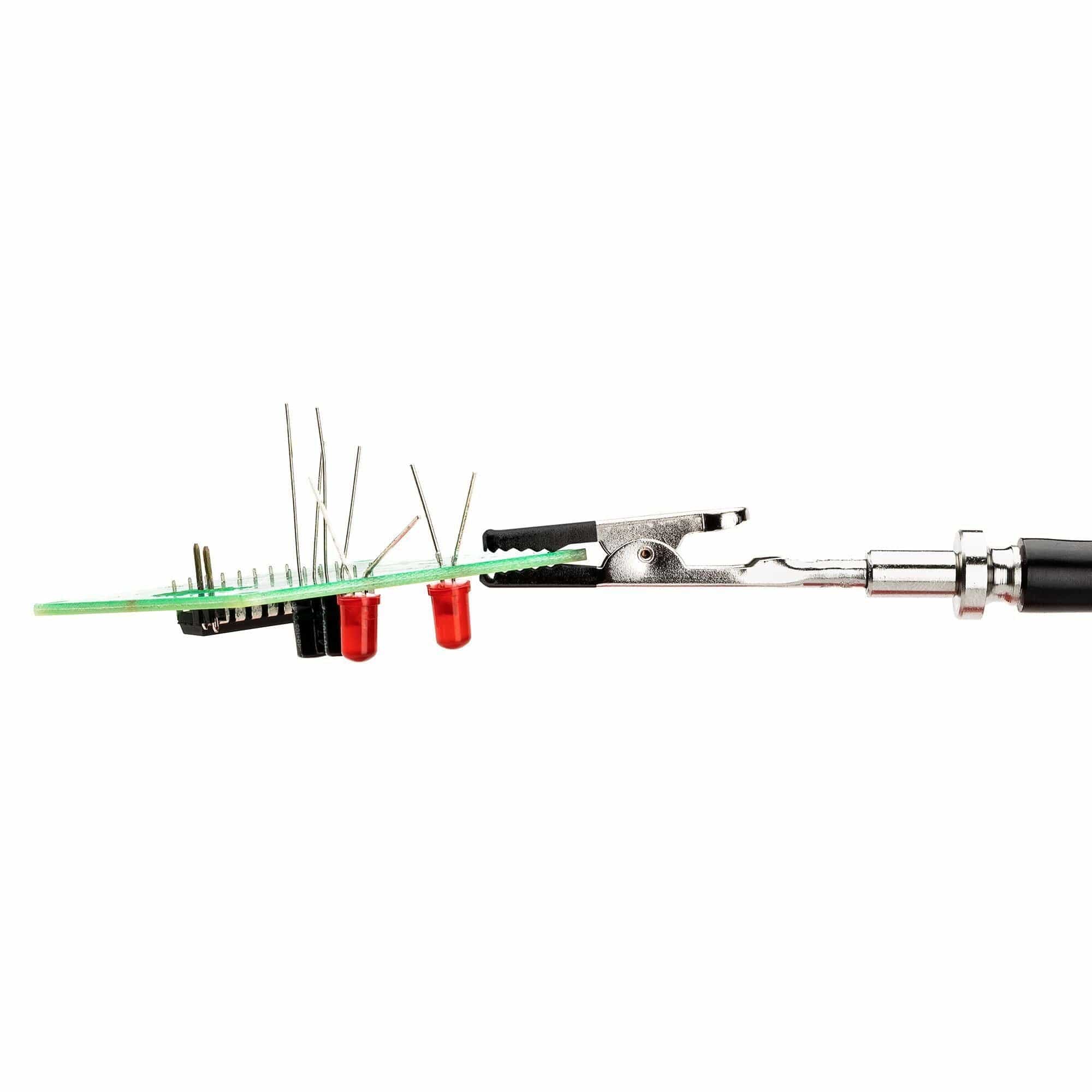 Close-up of PCB held by helping hands tool during soldering, showing red LEDs and soldering iron in use