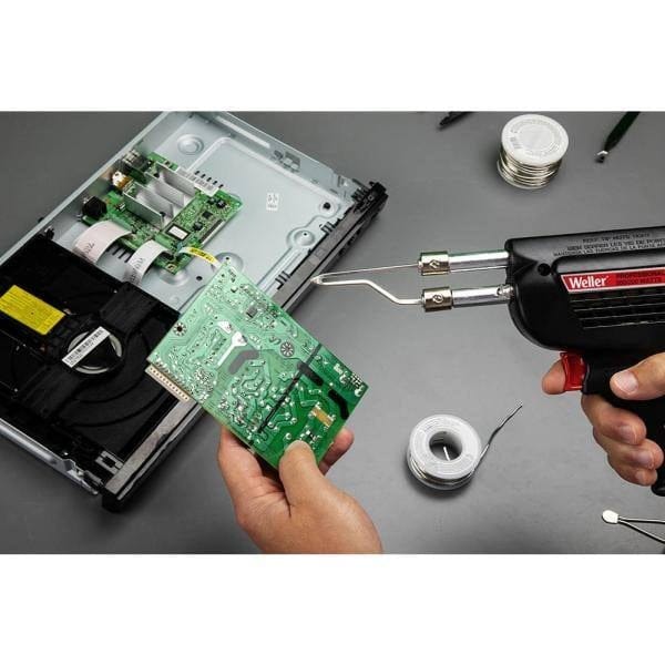 A hand holding the Weller D550 gun over an electronic assembly, showcasing the ergonomic pistol grip and the tool's portability for on-site industrial maintenance and electrical repairs.