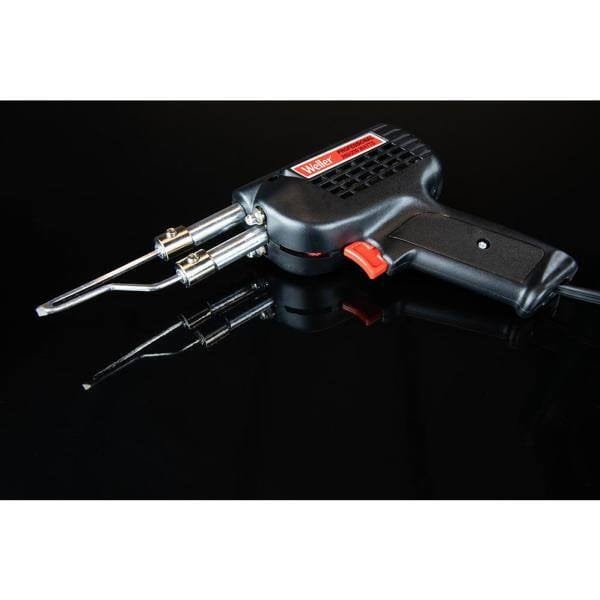 A high-contrast shot of the Weller D550 soldering gun resting on a reflective black surface, emphasizing the professional build quality and sleek industrial design of the dual-heat tool.
