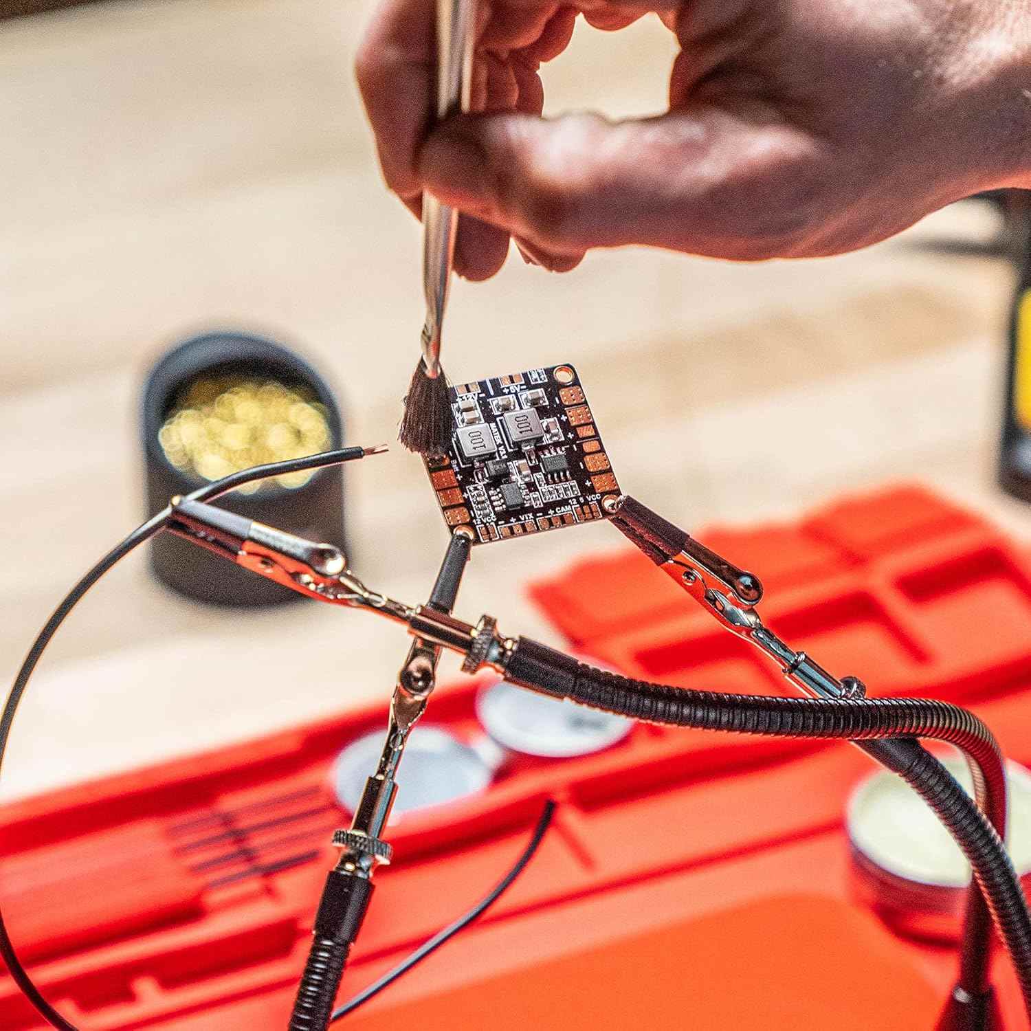 An action photo of a technician using the flux brush to prep a PCB board held by helping hands, demonstrating the professional utility of the Weller accessory kit in high-precision electronics work.