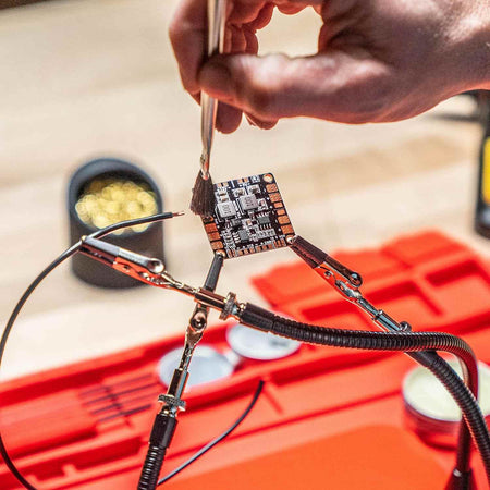 An action photo of a technician using the flux brush to prep a PCB board held by helping hands, demonstrating the professional utility of the Weller accessory kit in high-precision electronics work.