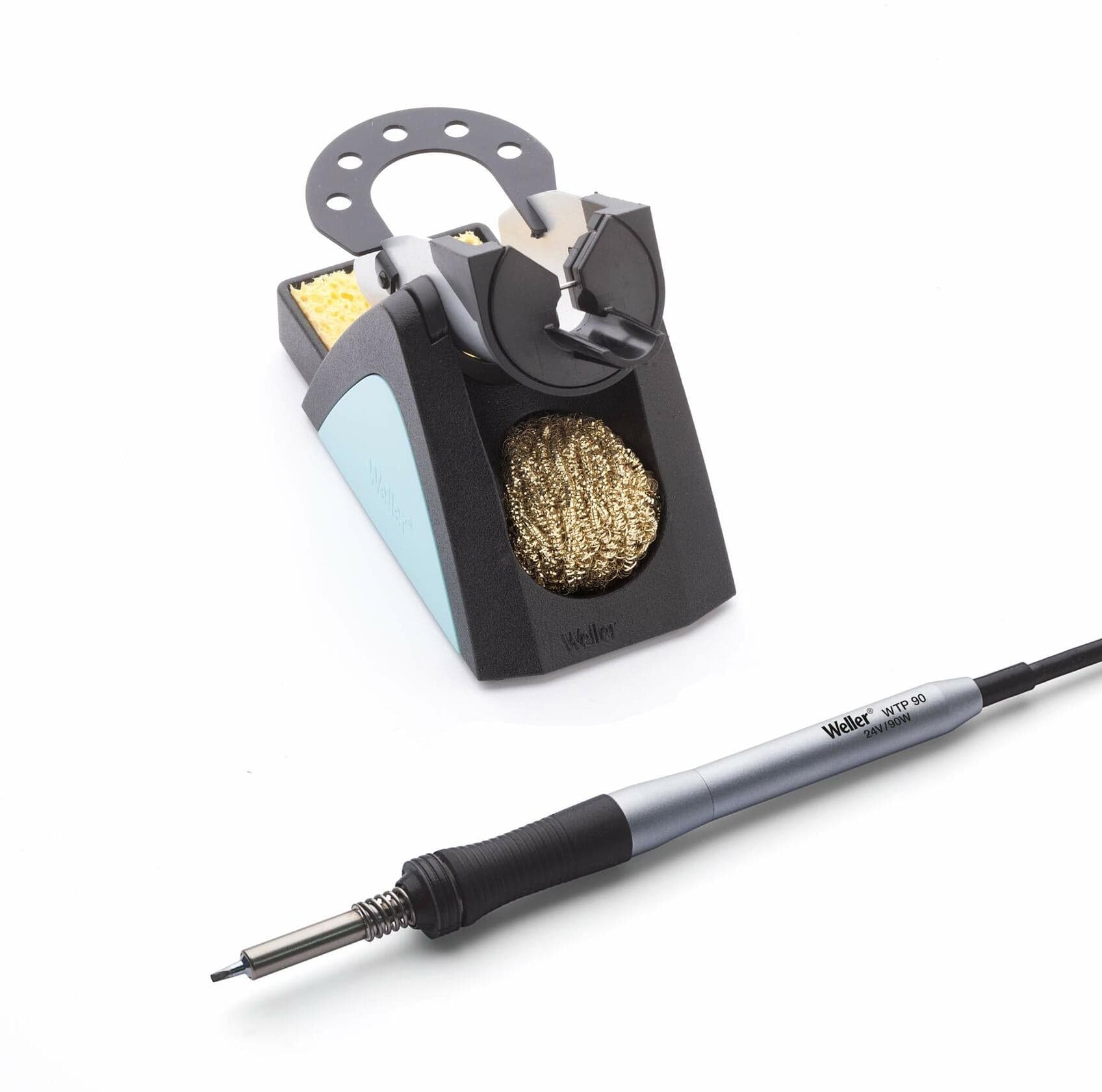Weller WTP90 soldering iron resting in a stand with brass wire sponge and yellow cleaning sponge. Both the iron and stand are branded “Weller.” Setup is designed for safe handling and tip cleaning during precision soldering tasks.