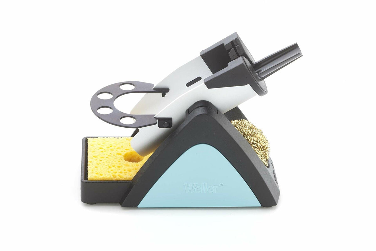 Weller soldering iron stand with metal holder, brass wire cleaner, and yellow sponge. The triangular base features a light blue panel labeled “Weller.” Designed to safely hold and clean soldering irons during electronics work.