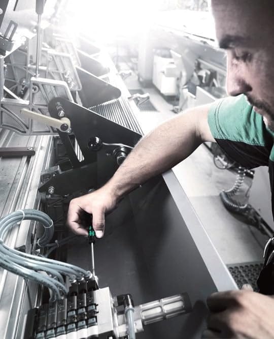 Person using a screwdriver to adjust industrial machinery with wires, connectors, and mechanical components in a workshop setting.