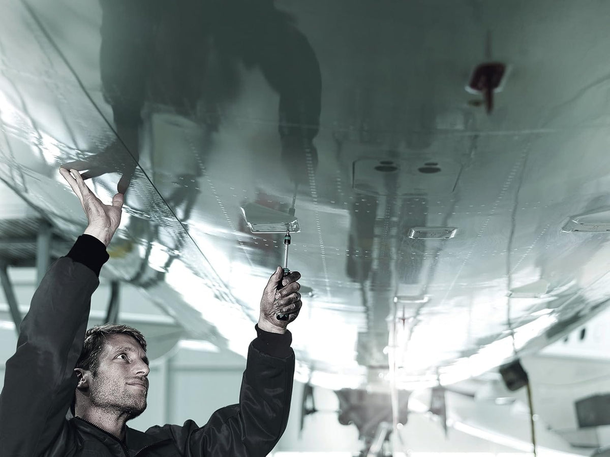 An application shot of a professional technician using the Wera Kraftform Kompakt 20 screwdriver to perform overhead maintenance on a polished metal aircraft surface.