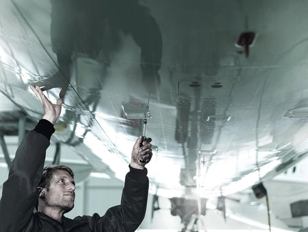 An application shot of a professional technician using the Wera Kraftform Kompakt 20 screwdriver to perform overhead maintenance on a polished metal aircraft surface.