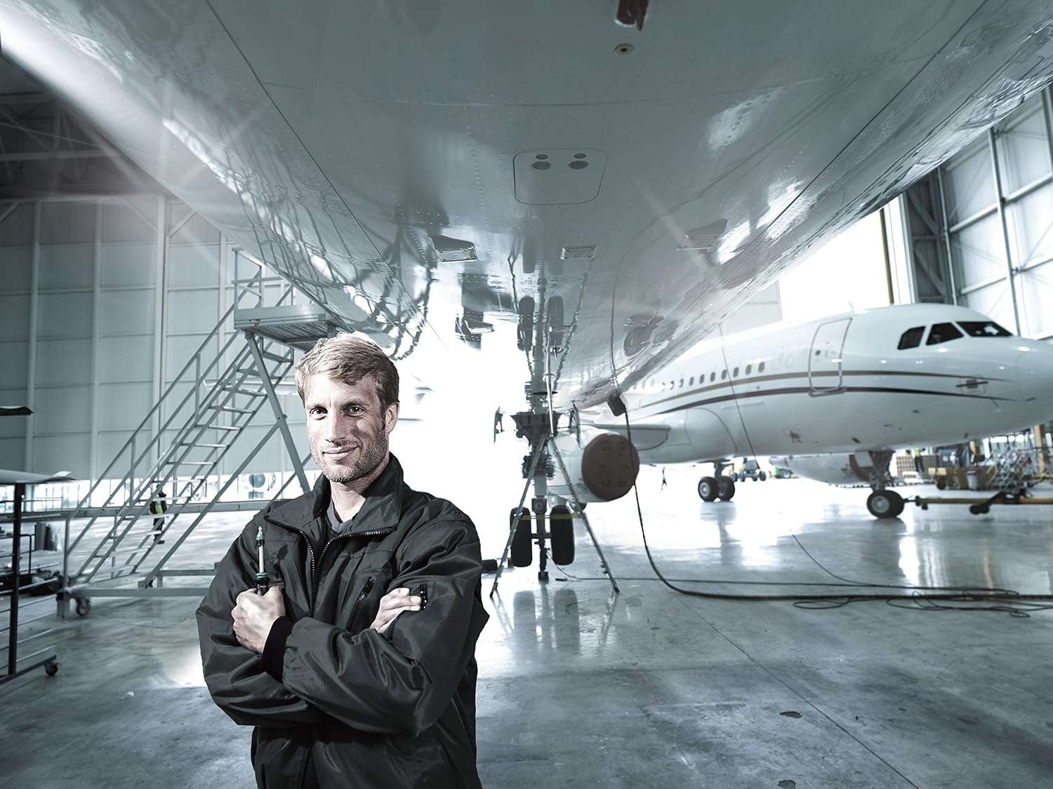Portrait of a professional mechanic smiling and holding the Wera Kraftform Kompakt 25 screwdriver, standing proudly inside a large aircraft hangar with an airplane in the background
