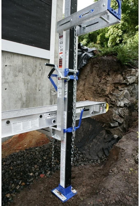 Close-up detail of the pump jack hoist supporting an aluminum stage platform next to a concrete wall, showing the crank handle and chain attachment.