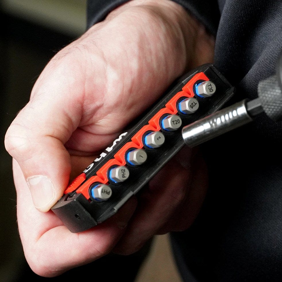 Hand holding a compact bit holder with labeled bits including PH1, PH2, T20, T25, and T30 near a power tool.