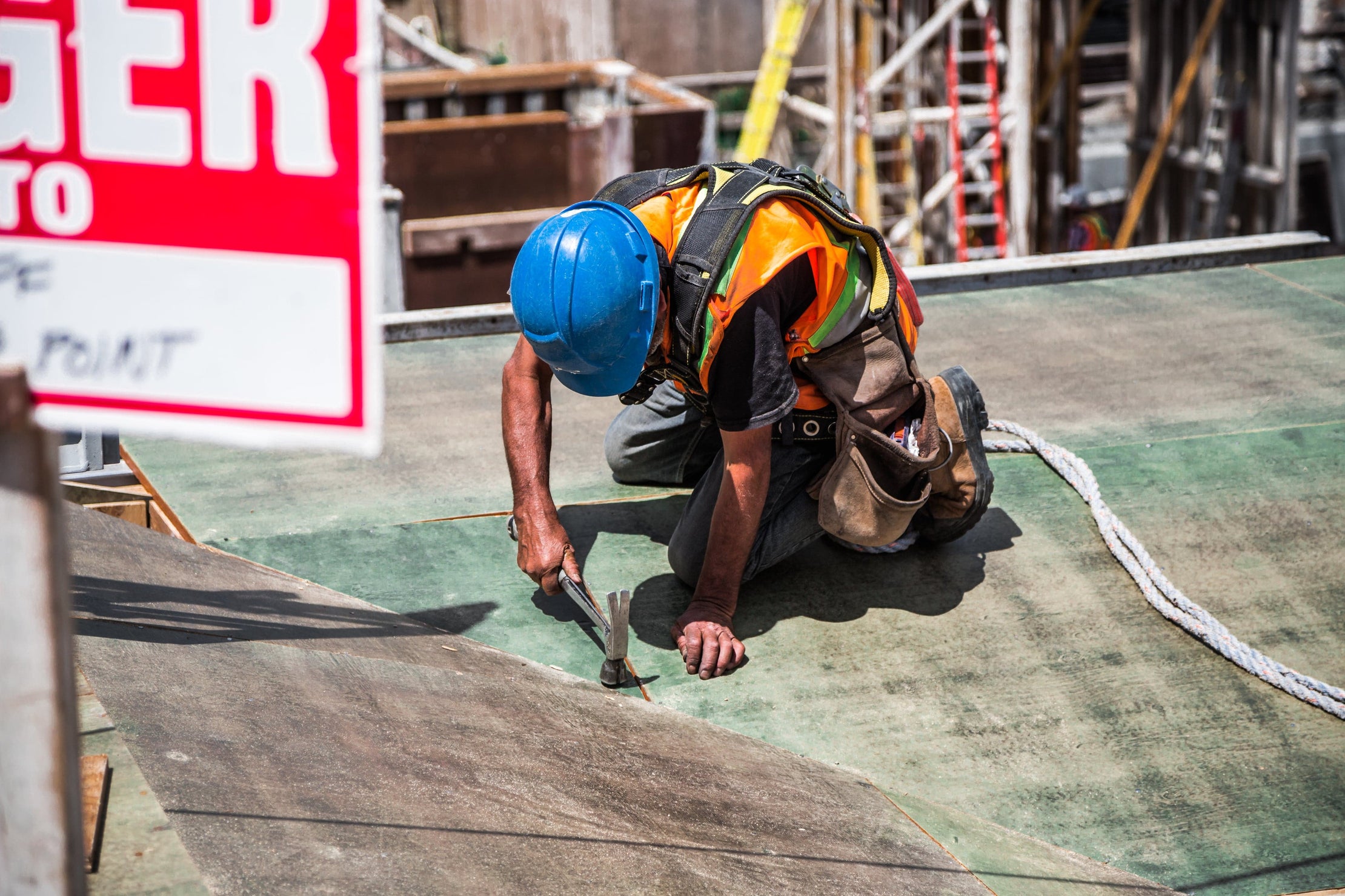 Construction worker repairing a roof with a hammer in full safety gear.