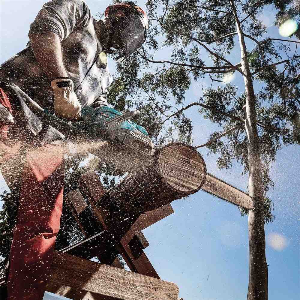 Load video: Person cutting a log with a chainsaw in a forest setting