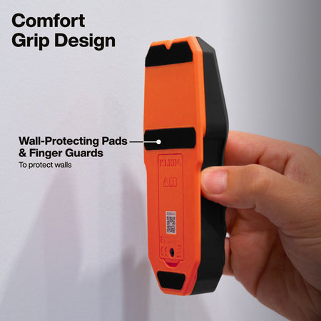 Hand holding Klein Tools ESF050 stud finder against a wall, showing black wall-protecting pads and finger guards on the back