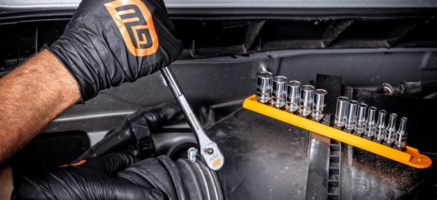 Load video: Person working on a car with tools and a socket set in a workshop setting