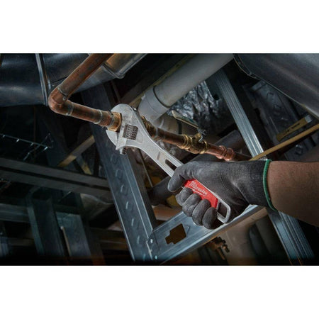 Low angle action shot of a gloved hand using the Milwaukee adjustable wrench to tighten a brass fitting on a copper pipe.