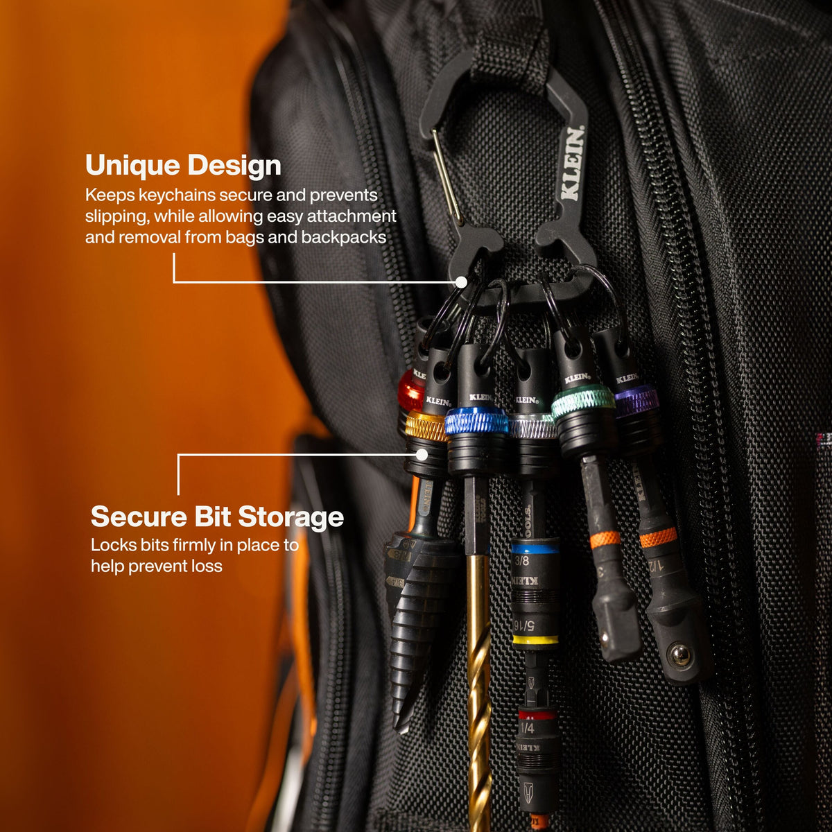 Close-up of a black backpack with a black carabiner holding a set of black keychain tools and bits. White text callouts with arrows explain the unique design and secure bit storage, against a dark backpack and warm orange background.