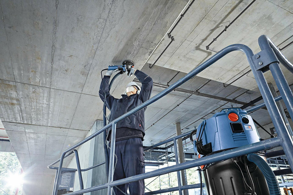 Worker using BOSCH DC4530HD 4-1/2 in. Turbo Row Diamond Cup Wheel to grind concrete ceiling.