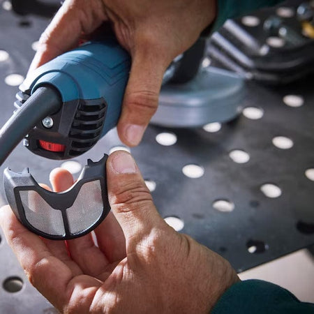 A close-up view of a person wearing green sleeves attaching a protective mesh dust filter to the rear air intake of the Bosch corded angle grinder.